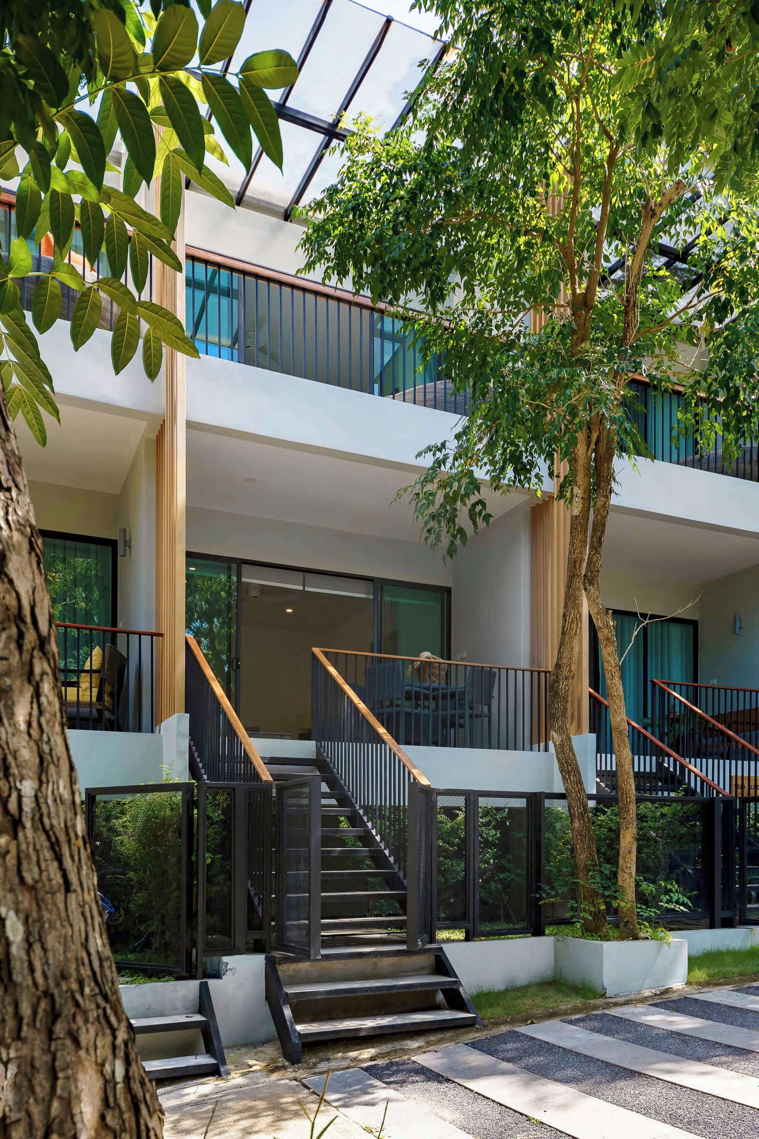 Un bâtiment moderne avec un escalier, des rampes de verre et un arbre au premier plan.