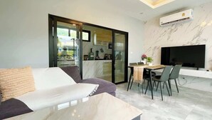 Ein modernes Wohnzimmer mit einer Couch, einem Esstisch mit Stühlen, einem an der Wand befestigten Fernseher und einer Schiebetür zu einer Küchenzeile.