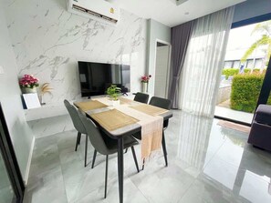 Ein moderner Essbereich mit Fernseher, einem Tisch mit Stühlen und Blick ins Freie.