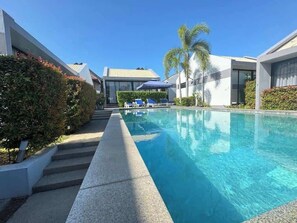 Ein modernes Hotel mit Swimmingpool, Liegestühlen und Palmen.