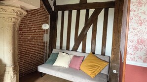 Een gezellige kamer met zichtbare houten balken, een bakstenen muur en een beklede bank met kussens.
