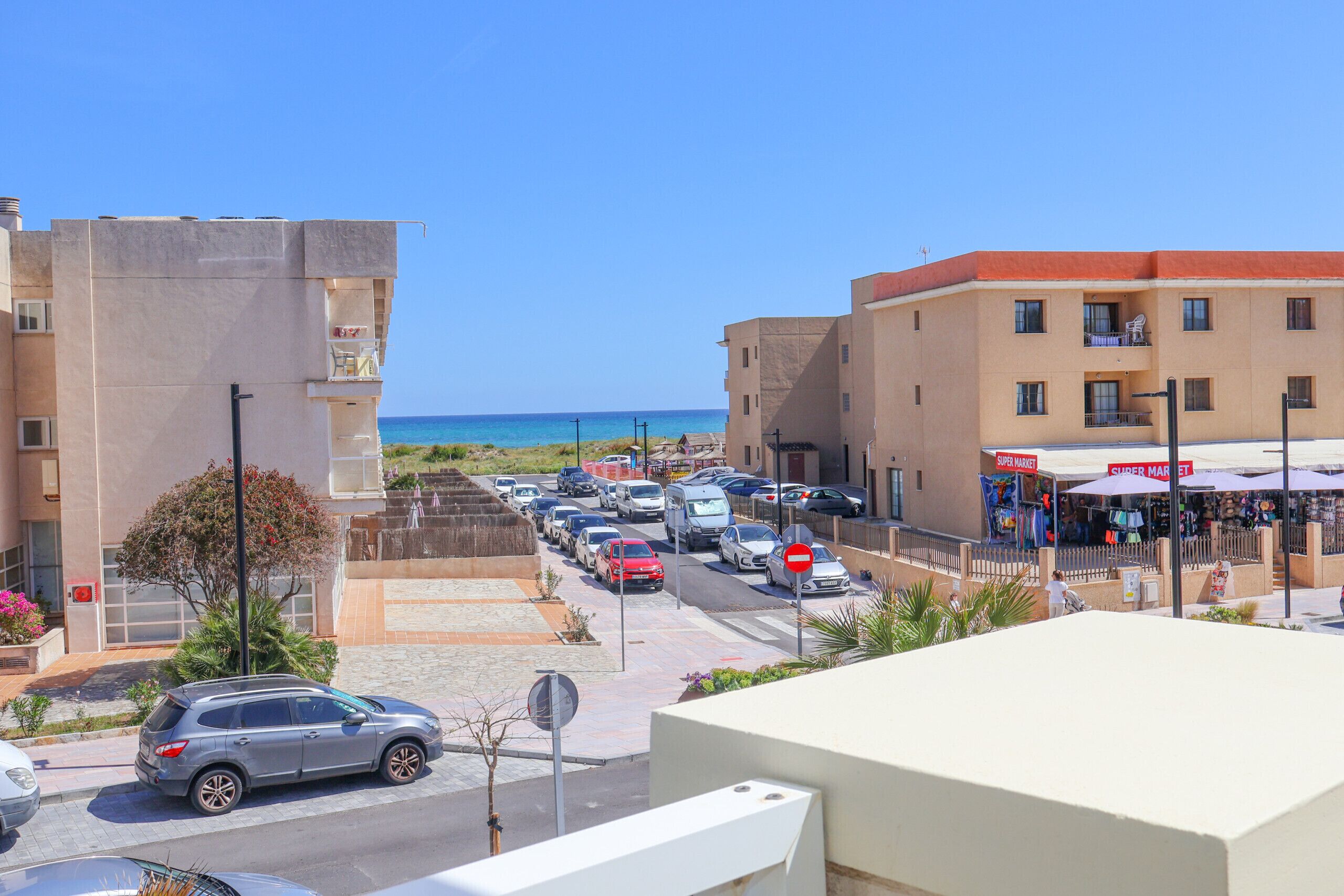 Une rue côtière bordée de voitures garées, avec un supermarché et une vue sur la mer.