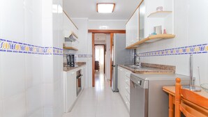 Cozinha estreita com armários brancos, bancada de granito e uma cadeira de madeira.