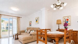 Uma sala de estar com sofá, mesa de jantar de madeira, cadeiras, um candelabro e obras de arte nas paredes.