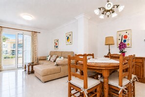 A living room with a sofa, wooden dining table, chairs, a chandelier, and artwork on the walls. - 284 La Santa by Mallorca Charme (Ca´n Picafort)