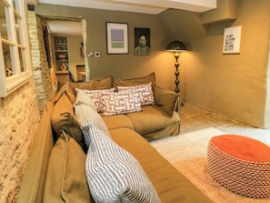 Ein gemütliches Wohnzimmer mit einer Couch, gemusterten Kissen, einer Lampe und einem gerahmten Kunstwerk an der Wand.
