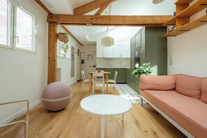 Ein modernes Interieur mit einem runden Tisch, einem rosa Sofa, Holzbalken und einer Küchenzeile.