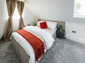 Ein Schlafzimmer mit Bett, Nachttisch, Lampe und Vorhängen.