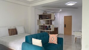 A bedroom with a bed, a teal sofa, a white desk, and a shelving unit.