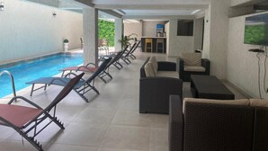 A poolside area with lounge chairs, a sofa, and a TV screen.