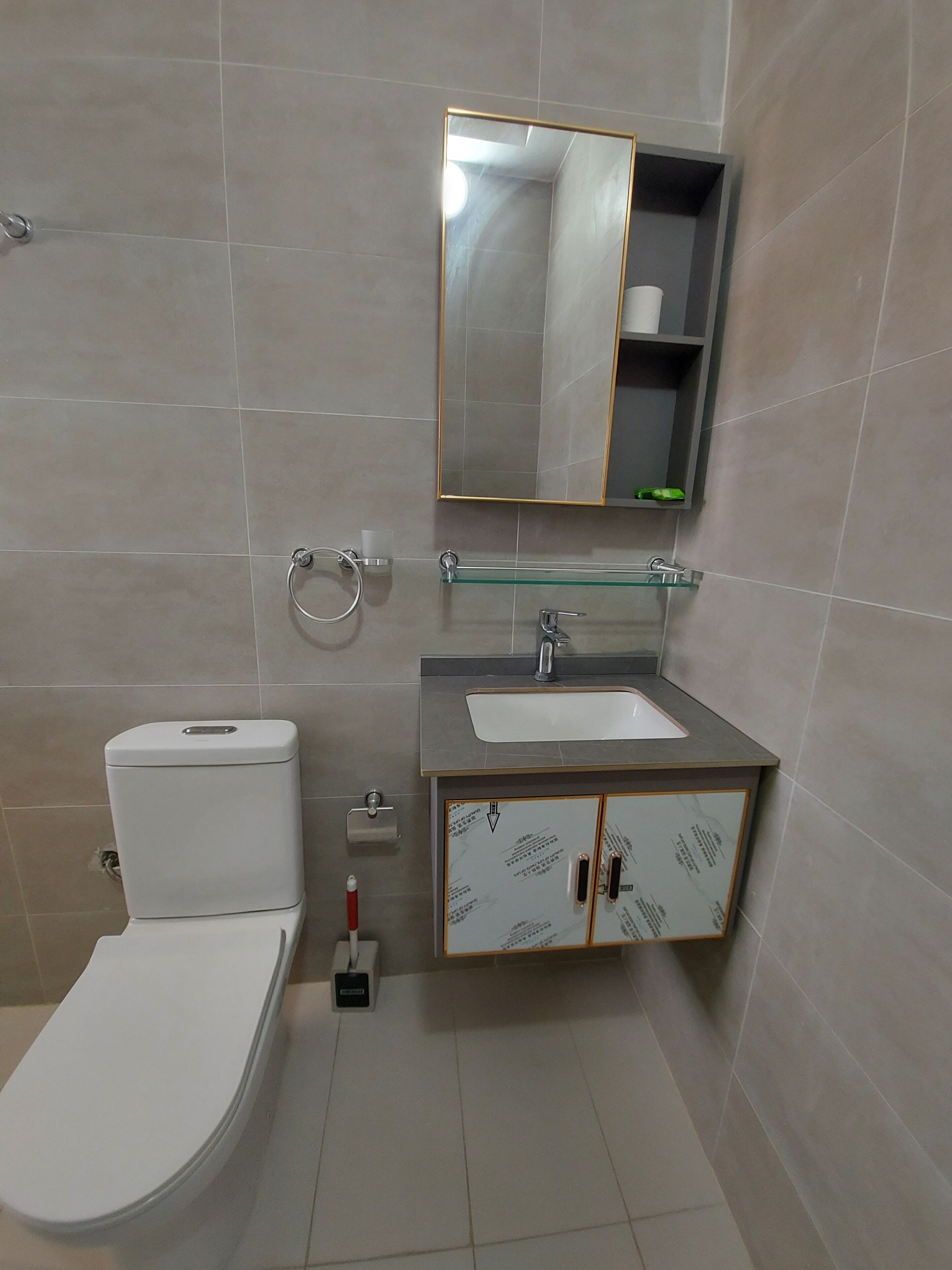 A bathroom with a toilet, sink, mirror, and glass shelf.