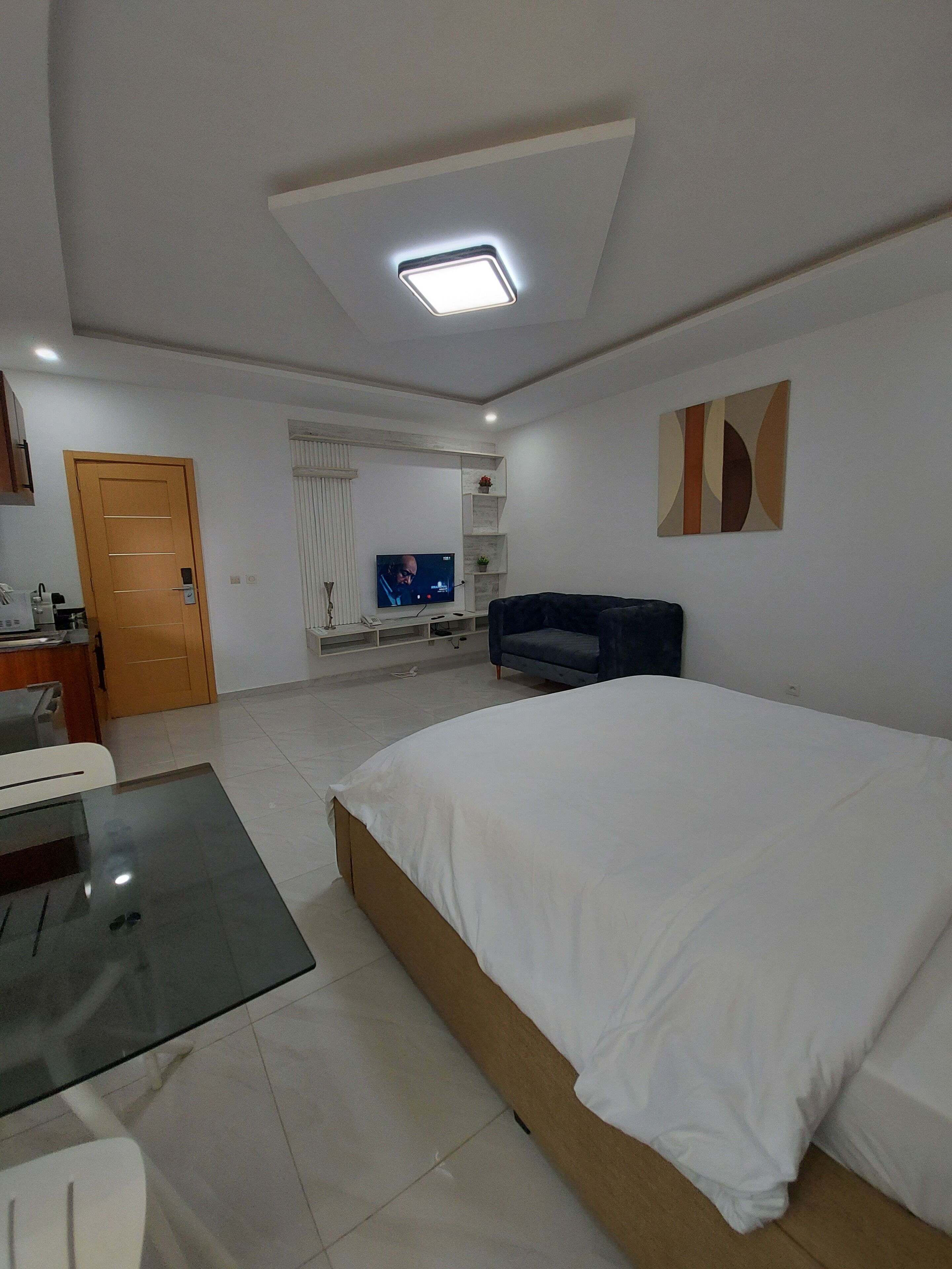 Quarto com cama, televisão, sofá, escrivaninha e porta.