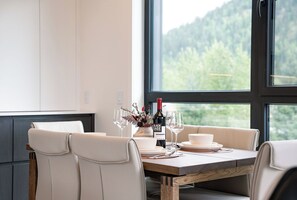 Ein Esstisch mit weißen Stühlen, einer Flasche Black Sage Wein und Gläsern.