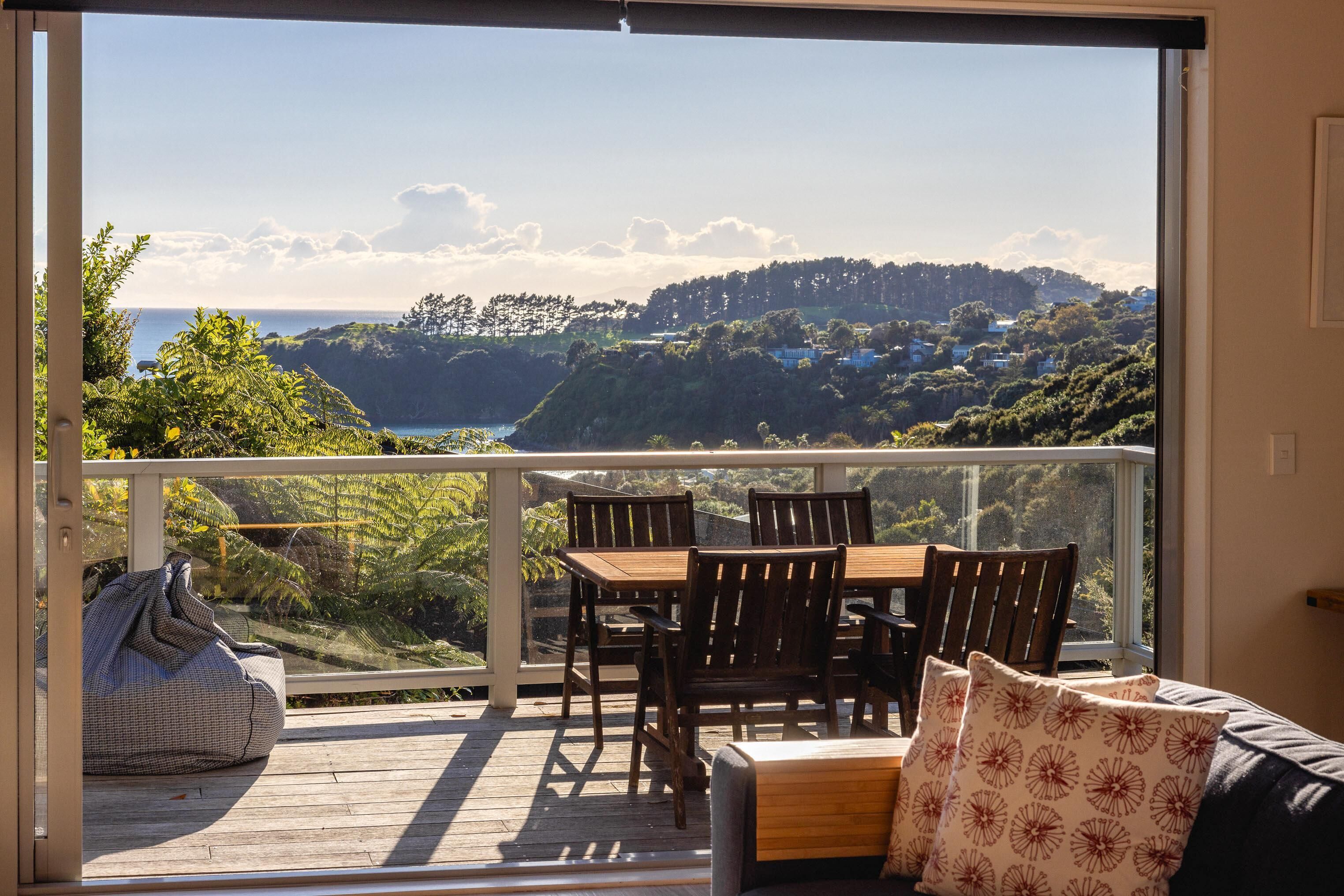 Un balcon avec une table et des chaises en bois, un fauteuil poire et une vue sur un paysage vallonné.