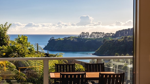 Een balkon met een tafel en stoelen, met uitzicht op een kustlandschap met bomen en zee.