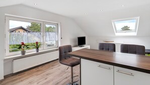 A modern kitchen with a wooden countertop, bar stools, a built-in TV, and large windows offering views of the outside. - Apartment 'Conny' with Mountain View, Balcony and Wi-Fi (Bühl)
