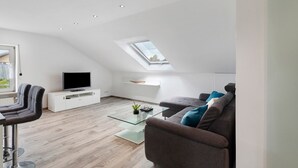 A modern living room with a glass coffee table, a sofa, a TV, and a skylight. - Apartment 'Conny' with Mountain View, Balcony and Wi-Fi (Bühl)