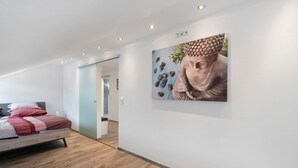 A modern hotel room with a wooden floor, a bed with red bedding, and a large Buddha statue on the wall. - Apartment 'Conny' with Mountain View, Balcony and Wi-Fi (Bühl)