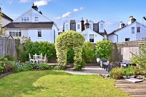 A residential garden with a wooden deck, white furniture, and a well-maintained lawn. - Finest Retreats | Yew Cottage (Tunbridge Wells)