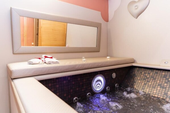 Un cuarto de spa con un jacuzzi, un espejo y toallas sobre el mostrador.