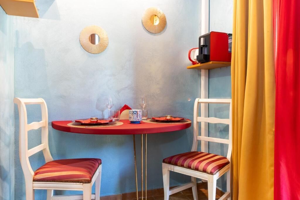 A dining area with a round table, two chairs, and a coffee machine on a shelf.
