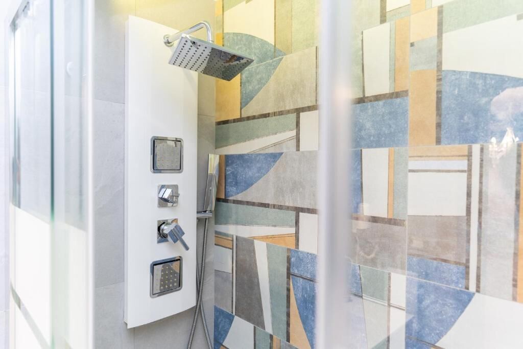 Ducha con cabezal de mano, panel de control con botones y cerramiento de vidrio.
