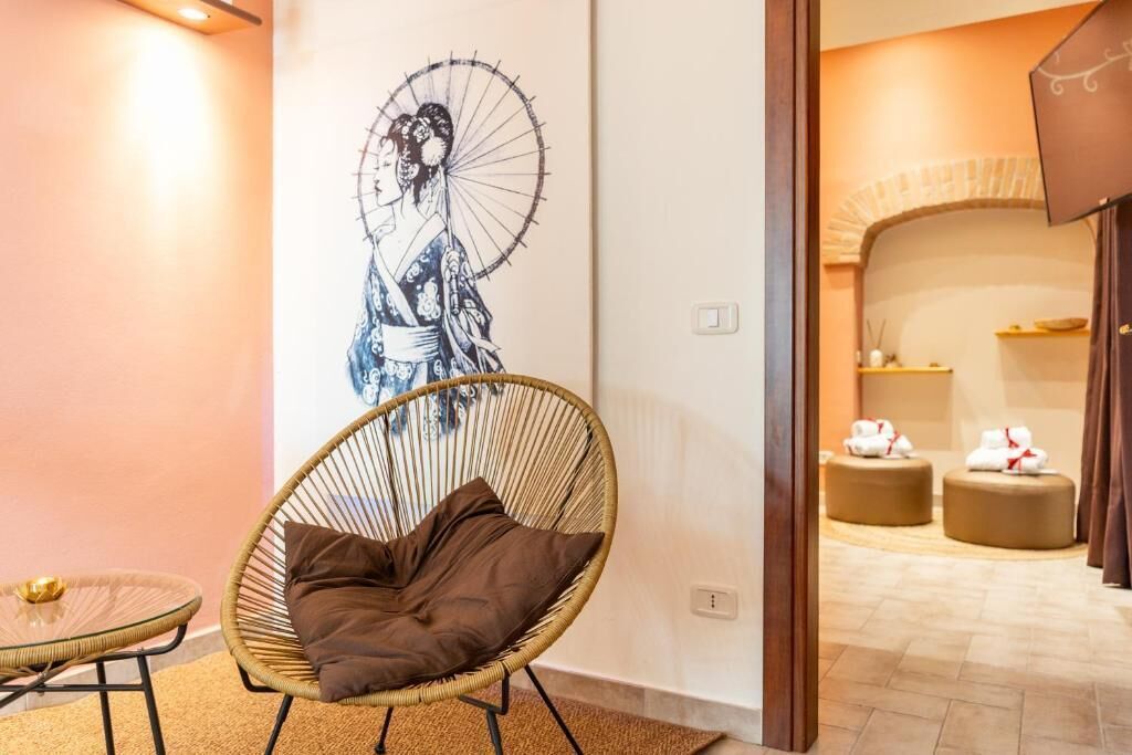 Una habitación con una silla de ratán, una mesa de vidrio, una obra de arte en la pared y una vista parcial de un área de spa.