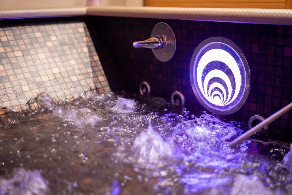 A hot tub with a circular light fixture and a tiled wall.