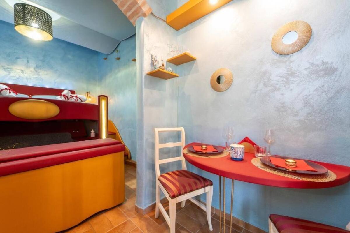 Una habitación con una cama, una mesa de comedor con sillas y un estante con objetos.