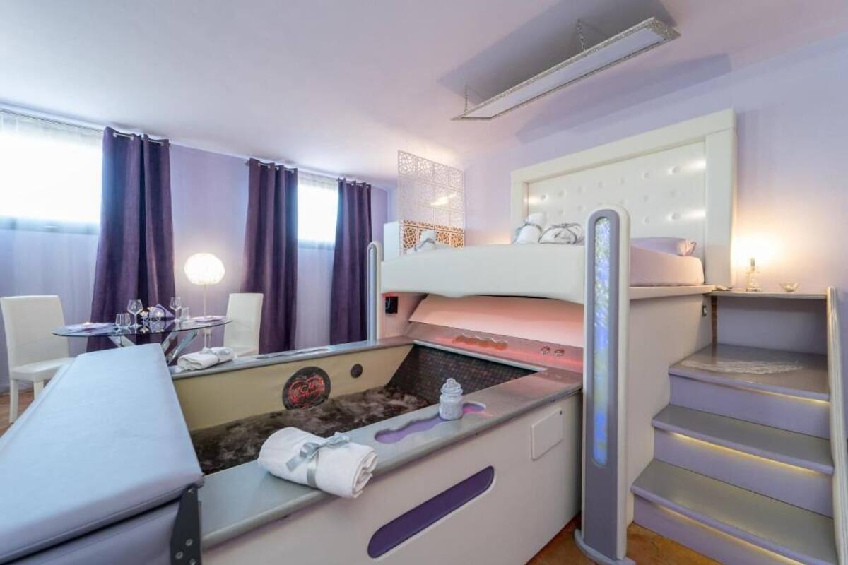Habitación de hotel con cama, mesa de masajes, una mesita con vasos, una silla y una escalera.