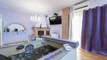 Una habitación con una bañera de hidromasaje de piedra, una chimenea, un televisor montado en la pared y una zona de ducha.