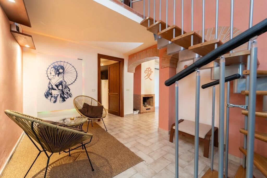 Una escalera con barandilla de metal, un muro con un mural y dos sillas de mimbre.