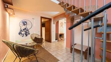 Un escalier avec une rampe en métal, un mur orné d’une fresque et deux fauteuils en osier.