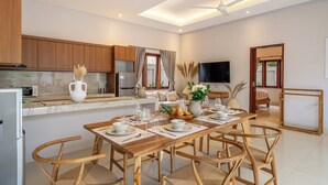 Uma cozinha moderna com armários de madeira, uma área de jantar com mesa e cadeiras de madeira, e uma TV de tela plana fixada na parede.