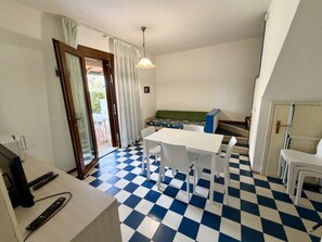 Ein gemütlicher Raum mit Schachbrettmuster auf dem Boden, einem Esstisch mit Stühlen, einer Küchenzeile und einem Fernseher.