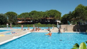 A swimming pool with people around it, surrounded by trees and buildings. - Lovely Villa With Pool, Garden and Fireplace (San Michele al Tagliamento)