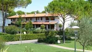 A two-story building with a tiled roof, surrounded by well-maintained hedges and a lawn. - Lovely Villa With Pool, Garden and Fireplace (San Michele al Tagliamento)