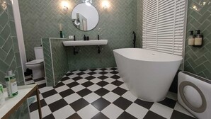 A bathroom with a checkered floor, a freestanding bathtub, a toilet, and a sink with a mirror above.