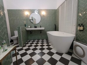 Ein Badezimmer mit Schachbrettboden, einer freistehenden Badewanne, einer Toilette und einem Waschbecken mit Spiegel darüber.