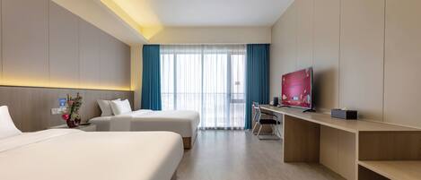 A hotel room with two beds, a desk, a TV, and a large window with curtains.