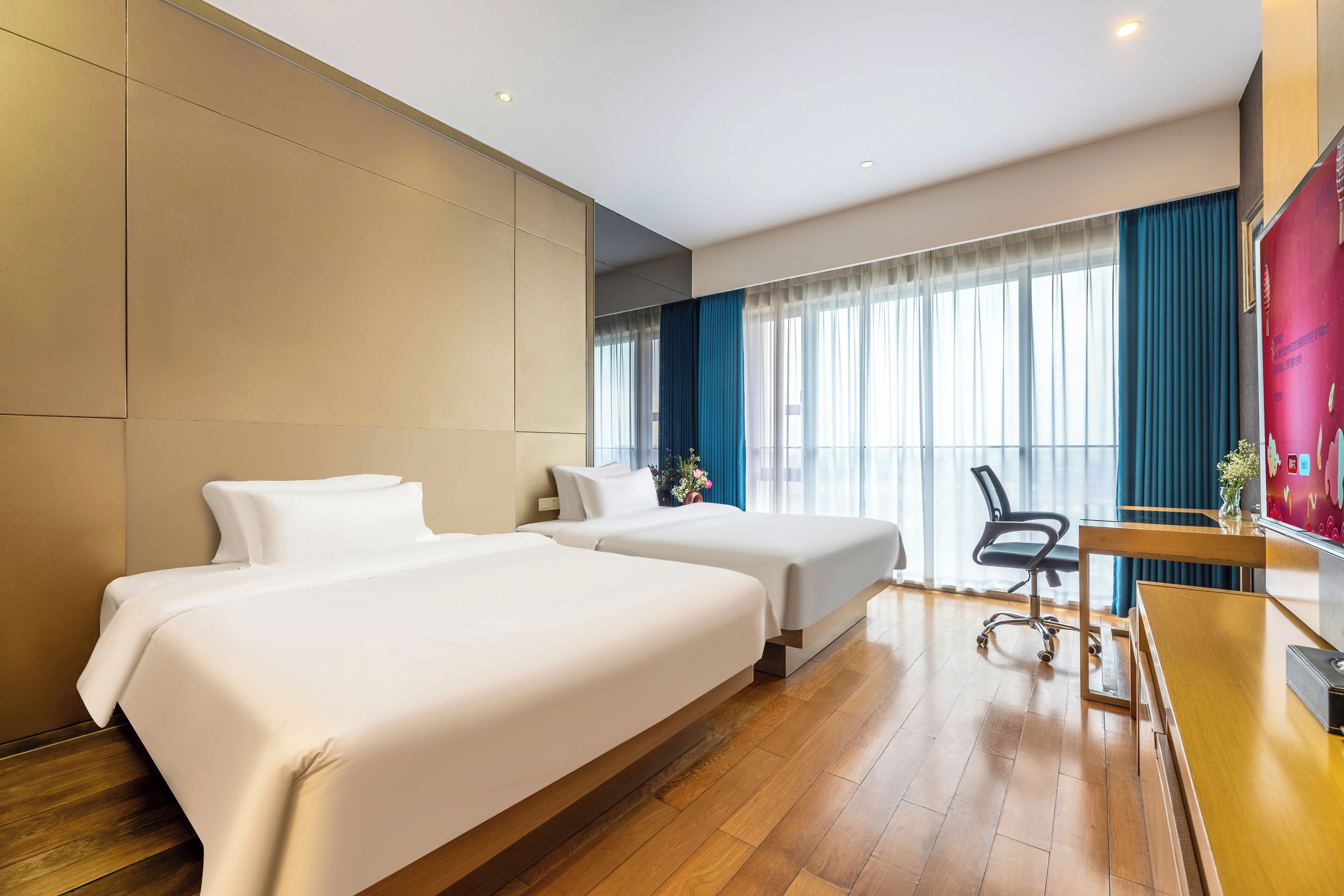 Een hotelkamer met twee bedden, een bureau, een stoel en een groot raam met gordijnen.
