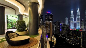 Ein Balkon mit Blick auf den Stadtpanoramablick, einschließlich der Petronas Towers, einer Topfpflanze und einem Korbstuhl.
