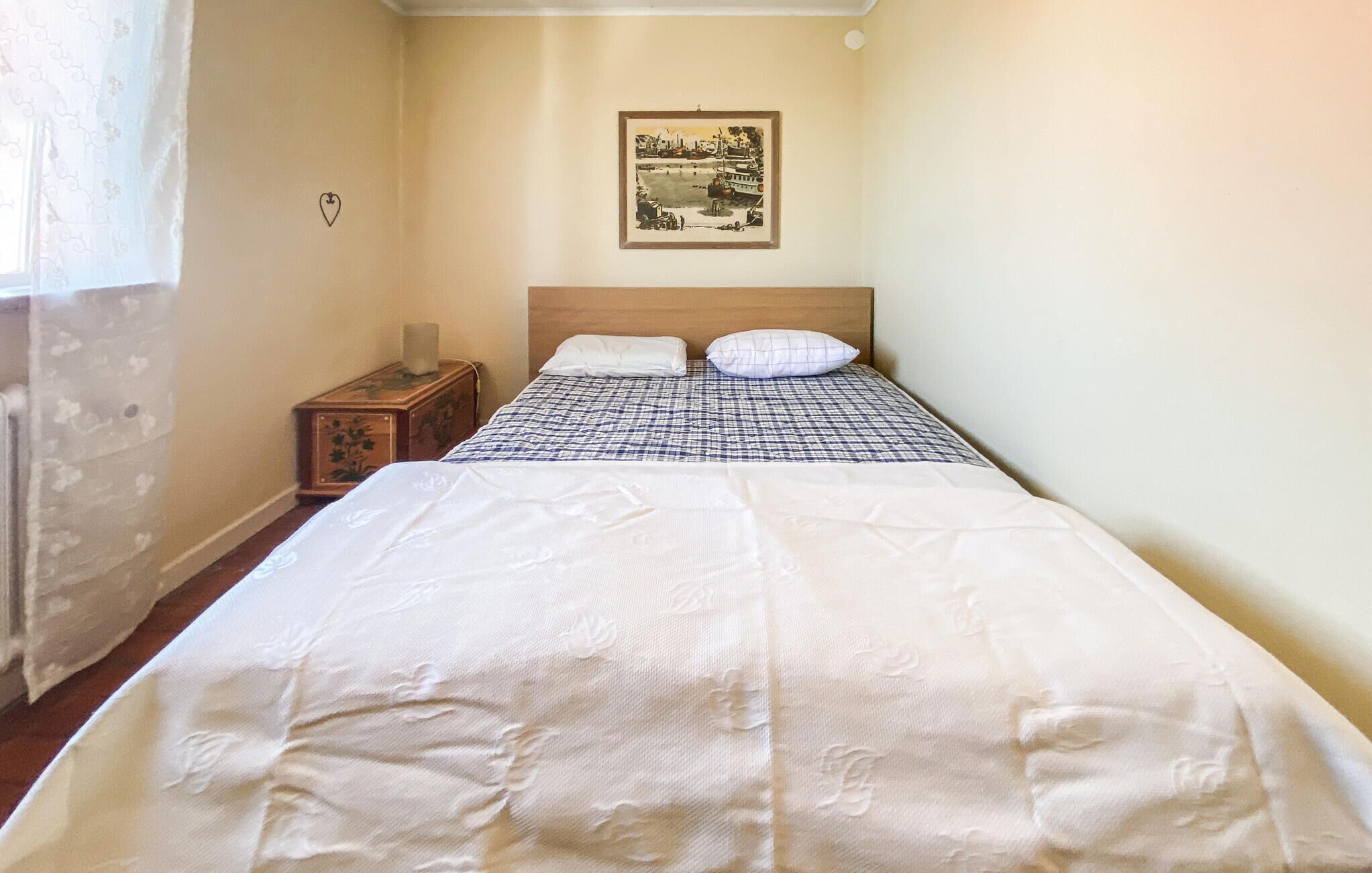 Een slaapkamer met een bed, een nachtkastje, een ingelijste foto aan de muur en een raam met gordijnen.