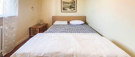 Een slaapkamer met een bed, een nachtkastje, een ingelijste foto aan de muur en een raam met gordijnen.