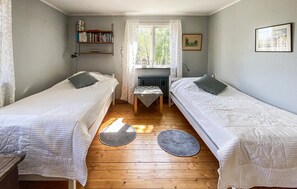 Une chambre avec deux lits simples, une petite table, une bibliothèque et une fenêtre avec des rideaux.