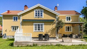 A two-story yellow house with a red-tiled roof, a covered porch, and a small garden area. - Nice home in Köpingsvik with sauna (Köpingsvik)