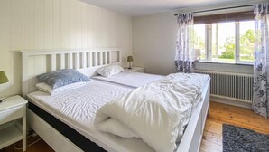 A double bed with white bedding, a nightstand with a lamp, a window with curtains, and a radiator. - Nice home in Köpingsvik with sauna (Köpingsvik)