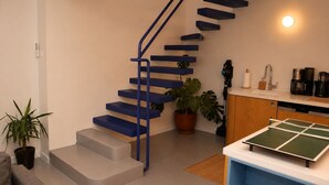 A staircase with blue steps and a handrail, a kitchen area with a coffee machine, and a ping pong table. - Ayvalık Center Modern Detached House in the City Center (Ayvalık)
