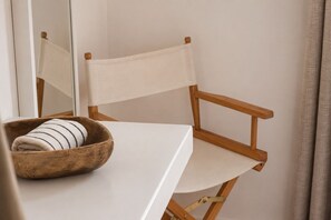A wooden chair with a white cushion, a wooden bowl with a striped pillow, and a white table.