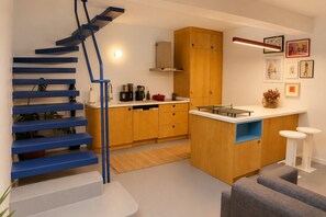 A modern kitchen with a wooden island, a blue staircase, and a small seating area.